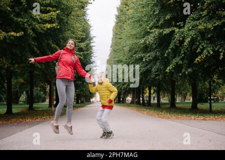 Madre e figlio saltano nel parco autunnale. Stagione autunnale. Felice giovane bella madre e suo figlio hanno una passeggiata nel parco Foto Stock