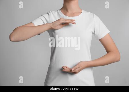 Donna che tiene le mani vicino al petto su sfondo grigio chiaro, primo piano Foto Stock