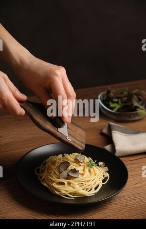 Donna affettare il tartufo su spaghetti a tavola di legno, primo piano Foto Stock