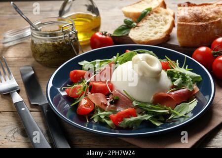 Deliziosa insalata di burrata con pomodori, prosciutto e rucola servita su un tavolo di legno Foto Stock