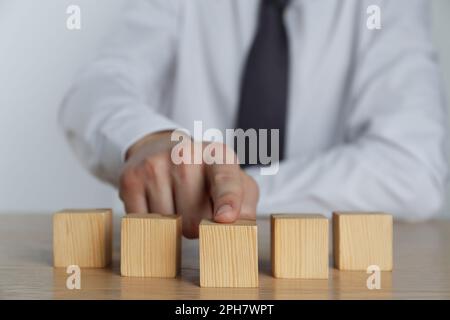 Uomo d'affari che organizza cubetti bianchi su un tavolo di legno, guardaroba. Spazio per il testo Foto Stock