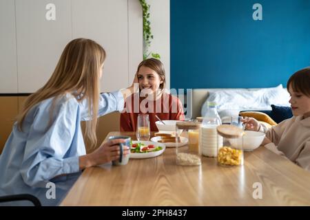Buona madre caucasica e due bambini che parlano e sorridono mentre fanno colazione insieme Foto Stock