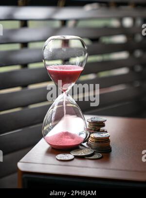 Sabbia che corre o che scorre giù di una clessidra con le monete accanto ad esso. Il tempo è concetto di denaro. Foto Stock