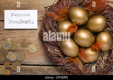 Molte uova d'oro, monete e carta con frase Pension investimenti su tavolo di legno, piatto Foto Stock