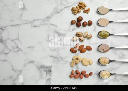 Vasetti con burro a base di frutta secca e ingredienti diversi su tavola in marmo bianco, piatto. Spazio per il testo Foto Stock