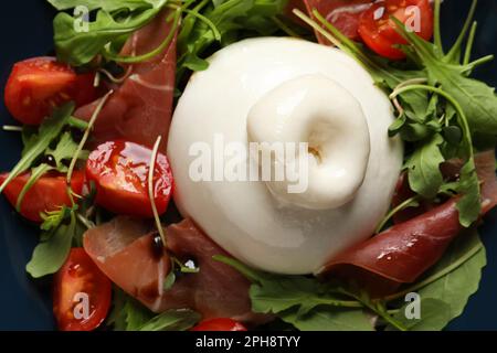 Deliziosa insalata di burrata con pomodori, prosciutto e rucola su piatto, primo piano Foto Stock