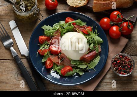 Deliziosa insalata di burrata con pomodori, prosciutto e rucola servita su tavolo di legno, piatto Foto Stock