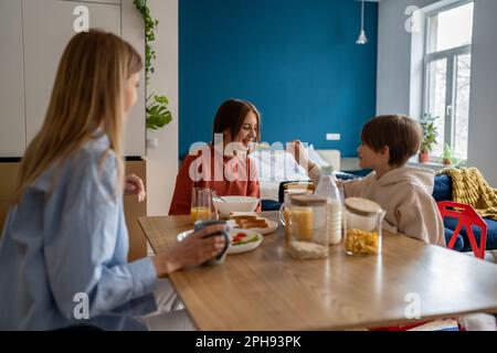 I fratelli e le sorelle dei bambini felici hanno divertimento mentre mangiano i cereali la mattina nel paese Foto Stock