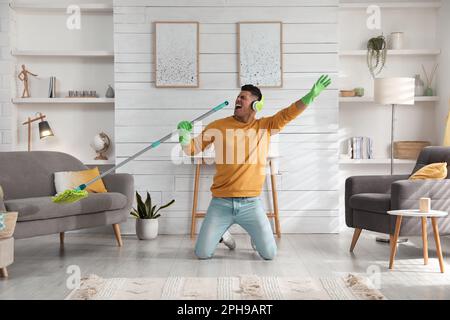 Uomo in cuffia con mop cantare mentre si pulisce a casa Foto Stock
