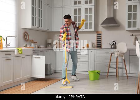 Uomo con il mop che canta mentre pulisce a casa Foto Stock