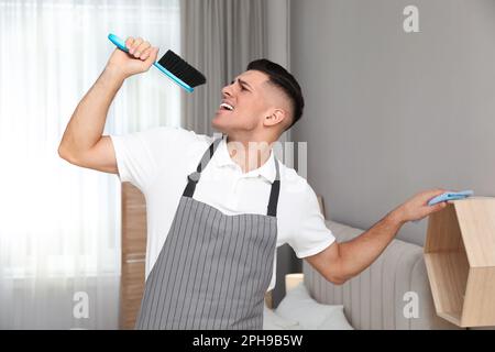 Uomo con spazzola e straccio che canta mentre pulisce a casa Foto Stock