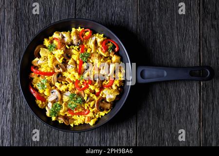 Chicken Paella of arborio rice, chicken fillet, mushrooms, julienned bell pepper and spices on a skillet on dark wood table, overhead view, flat lay Stock Photo