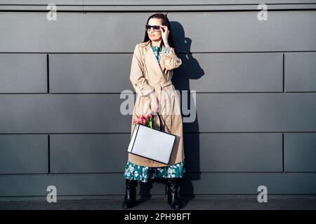 Lifestyle mockup Donna che trasporta una borsa di carta minimal. Donna che tiene bianco shopping eco borsa contro città sfondo. Borsetta vuota Foto Stock