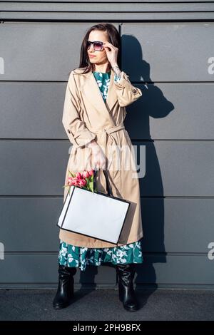 Lifestyle mockup Donna che trasporta una borsa di carta minimal. Donna che tiene bianco shopping eco borsa contro città sfondo. Borsetta vuota Foto Stock