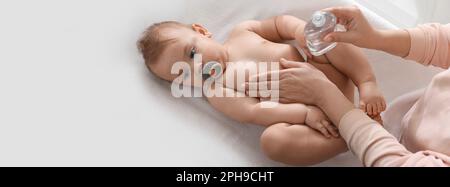 Madre massaggiando il suo bambino carino con olio sul tavolo cambiante, vista dall'alto. Design banner con spazio per il testo Foto Stock