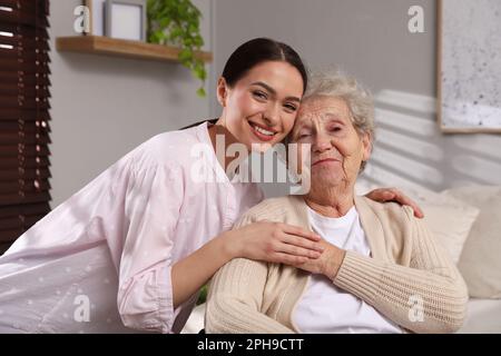 Ritratto di giovane caregiver e donna anziana al chiuso. Assistenza domiciliare Foto Stock