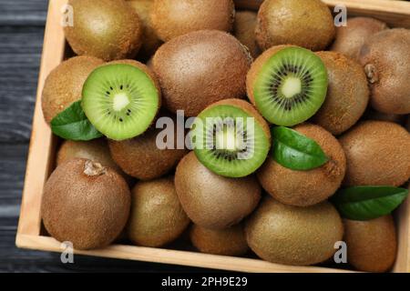 Cassa con taglio e kiwi interi freschi su tavolo di legno nero, vista dall'alto Foto Stock