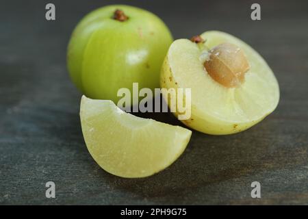 Primo piano della sezione fresca di Amla Berry con frutta intera su fondo di legno nero Foto Stock