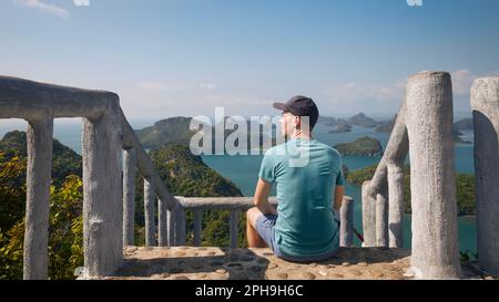 Uomo seduto su una scala in collina e guardando il mare con il gruppo belle isole tropicali. Ang Thong National Marine Park vicino a Koh Samui in Thailandia. Foto Stock