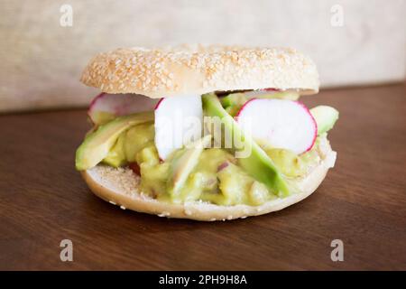 Delizioso panino all'avocado su pane in bagel. Un bagel è un pane tradizionalmente fatto di farina di grano e di solito ha un buco al centro. Foto Stock