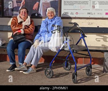 Due Signore che godono di un soleggiato rifugio dal vento, Llandudno Promenade, Conwy, Galles del Nord, Regno Unito, LL30 2LP Foto Stock