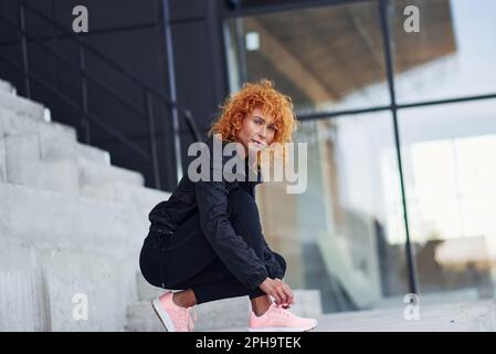 Giovane donna europea a testa rossa in abiti sportivi che indossano scarpe all'aperto Foto Stock