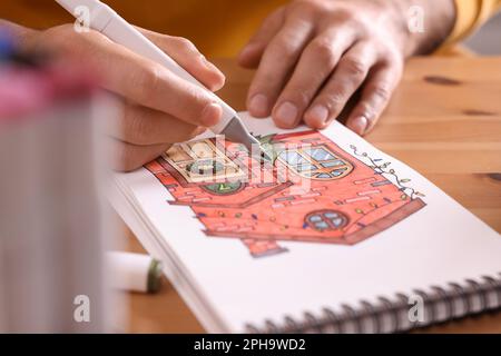 Uomo disegno in un libro di disegno con pennarello a tavola di legno, primo piano Foto Stock