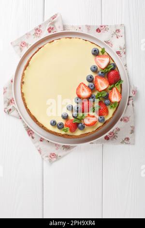 Classica cheesecake newyorkese fresca con frutti di bosco freschi e primo piano alla menta sul piatto del tavolo di legno. Vista verticale dall'alto Foto Stock