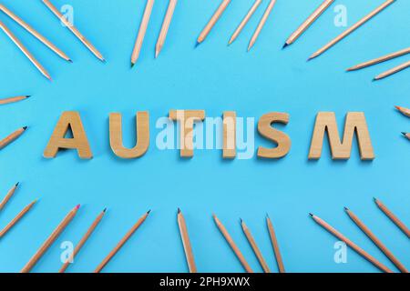 Composizione piatta con parola autismo e matite su sfondo azzurro Foto Stock