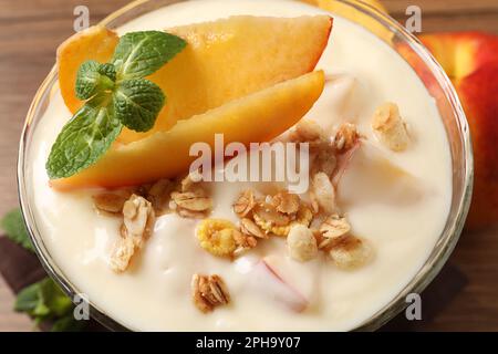 Gustoso yogurt alla pesca con muesli, menta e frutta in ciotola da dessert sul tavolo, primo piano Foto Stock