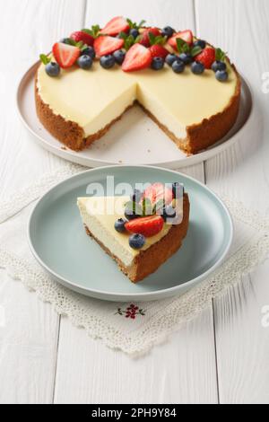 Classica cheesecake newyorkese fresca con frutti di bosco freschi e primo piano alla menta sul piatto del tavolo di legno. Verticale Foto Stock