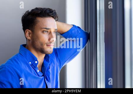 Felice uomo biraciale che si appoggia e guarda via, fuori dalla finestra Foto Stock