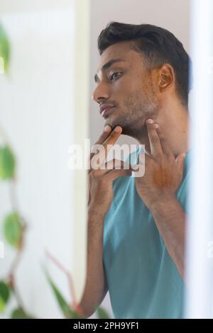 L'uomo biraciale toccava il viso e guardava la mascella nello specchio del bagno Foto Stock