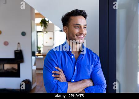 Felice uomo biraciale appoggiato alla finestra e guardando via Foto Stock