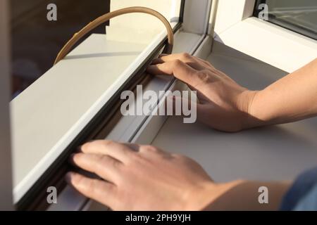 Operai edili che mettono nastro di gommapiuma sigillante su finestra, primo piano Foto Stock