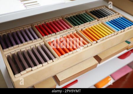 Scatola in legno con tavolette colorate e altri giocattoli montessori su scaffali Foto Stock