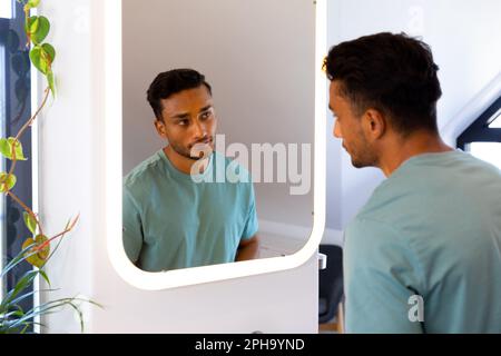 Uomo biraciale che guarda se stesso nello specchio del bagno Foto Stock