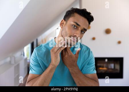 L'uomo biraciale toccava il viso, guardandosi nello specchio del bagno Foto Stock