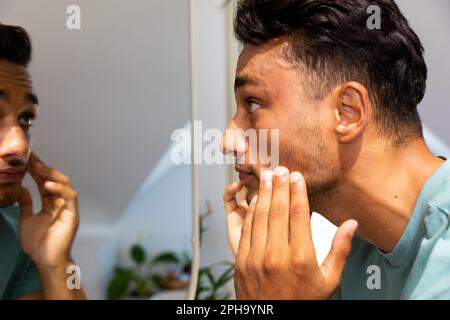 L'uomo biraciale toccava il viso, guardandosi nello specchio del bagno Foto Stock