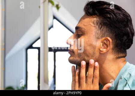 L'uomo biraciale toccava il viso, guardandosi nello specchio del bagno Foto Stock