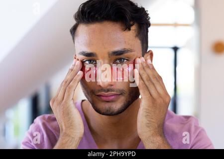 Felice uomo biraciale che applica sotto le maschere dell'occhio in bagno Foto Stock