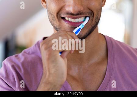 Sorridente uomo biraciale spazzolando i denti in bagno Foto Stock