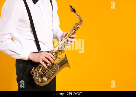 Uomo in elegante vestito con sassofono su sfondo giallo, primo piano. Spazio per il testo Foto Stock