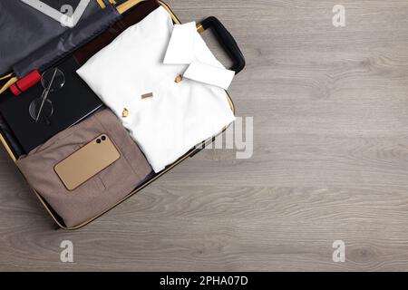 Vestiti e accessori piegati in valigia aperta su sfondo di legno, vista dall'alto con spazio per il testo. Preparativi per i viaggi di lavoro Foto Stock