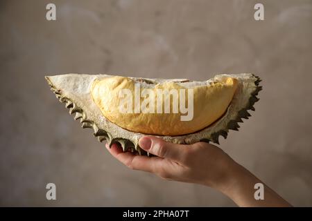 Donna che tiene pezzo di frutta dura matura su sfondo grigio, primo piano Foto Stock