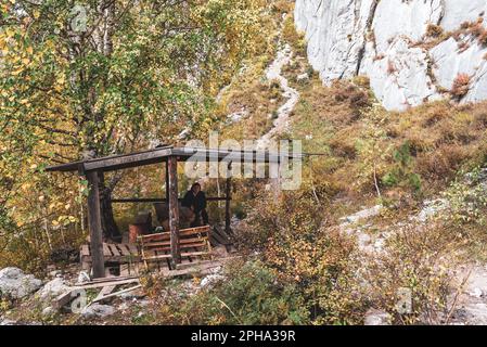 Una donna anziana turista siede riposante in un gazebo di legno sotto una montagna in Altai in Siberia. Foto Stock