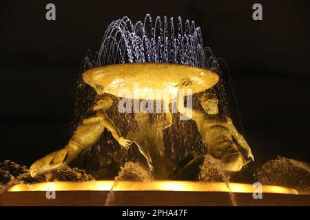 La Fontana dei Tritoni (di notte) è una fontana situata appena fuori la porta della città di la Valletta, Malta. Si compone di tre Tritoni di bronzo che sorreggono un'ampia vasca, equilibrata su una base concentrica costruita in cemento e ricoperti di lastre di travertino. La fontana è uno dei più importanti monumenti modernisti di Malta. Progettato e costruito tra il 1952 e il 1959. Il terminal degli autobus e la stazione si trovano nelle vicinanze. Foto Stock