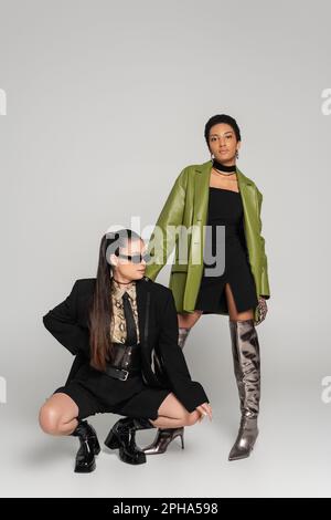 Trendy girlfriends interracial nei vestiti di molla che posano su fondo grigio, immagine di riserva Foto Stock