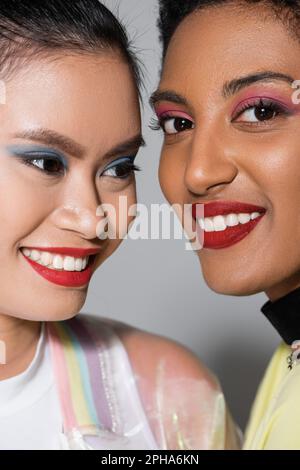Vista ravvicinata di modelli interracial sorridenti con labbra rosse e visage su sfondo grigio, immagine stock Foto Stock