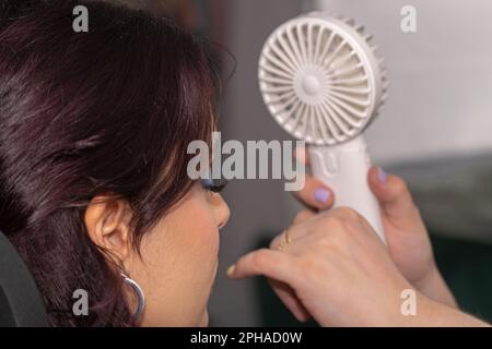 Giovane donna in un salone di bellezza che riceve aria da un piccolo ventilatore per asciugare le sue false ciglia Foto Stock